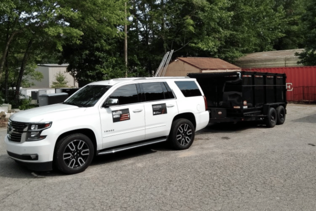 White Chevrolet Suburban owned by Majestic Mobile Junk Removal. It has a junk removal trailer attached, with business decals on the side.